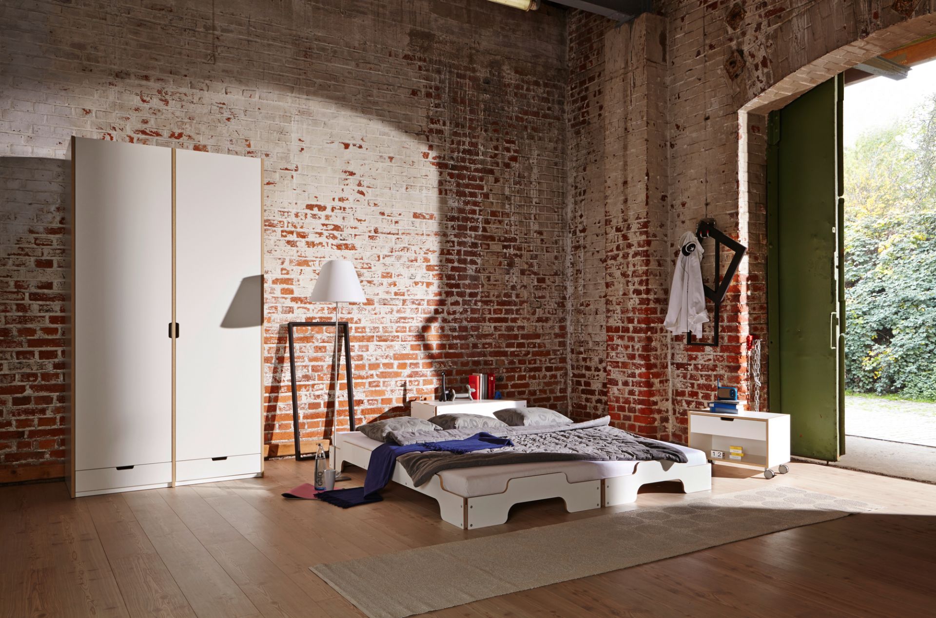 Helles Zimmer mit weißer Stapelliege von Müller Möbelwerkstätten, Kleiderschrank und Ziegelwand. Modernes Bett im Loft.