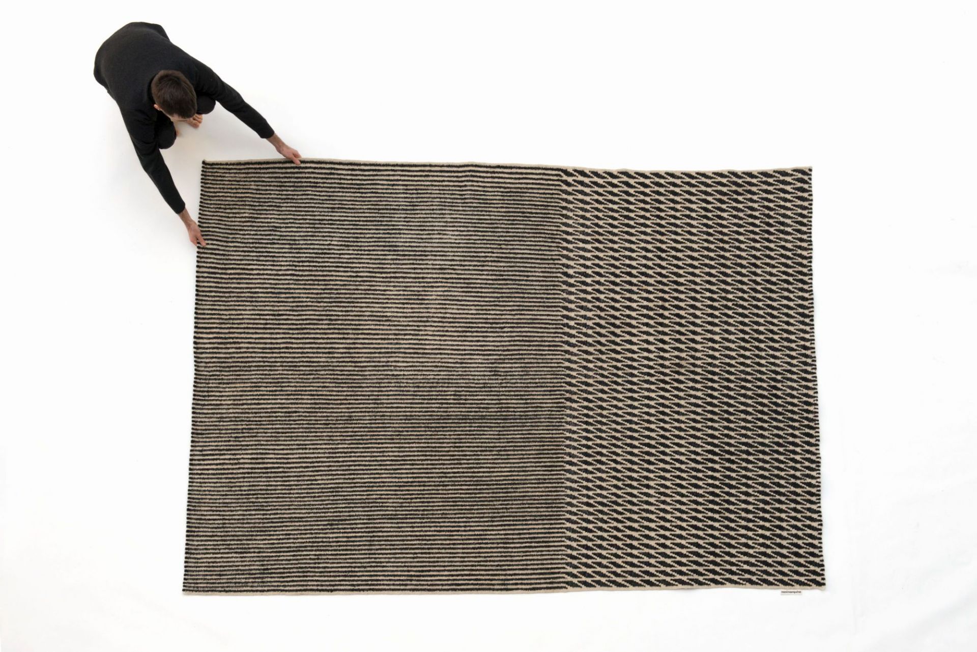 Draufsicht: Person rollt den modernen Nanimarquina Blur Teppich mit abstraktem Muster aus.