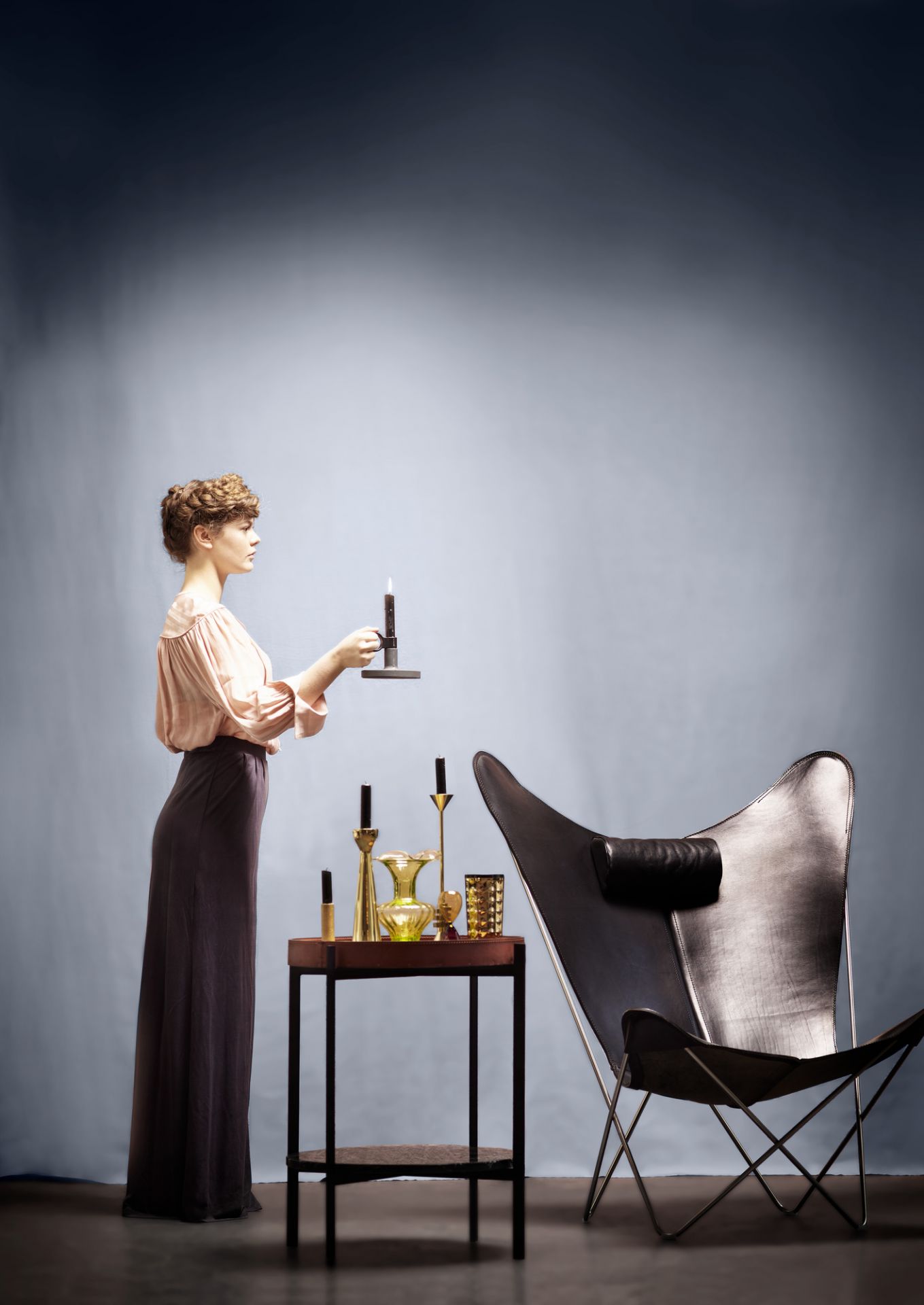 Frau zündet Kerze auf Deck Beistelltisch von Ox Denmarq an, Leder und Holz, neben Sessel.