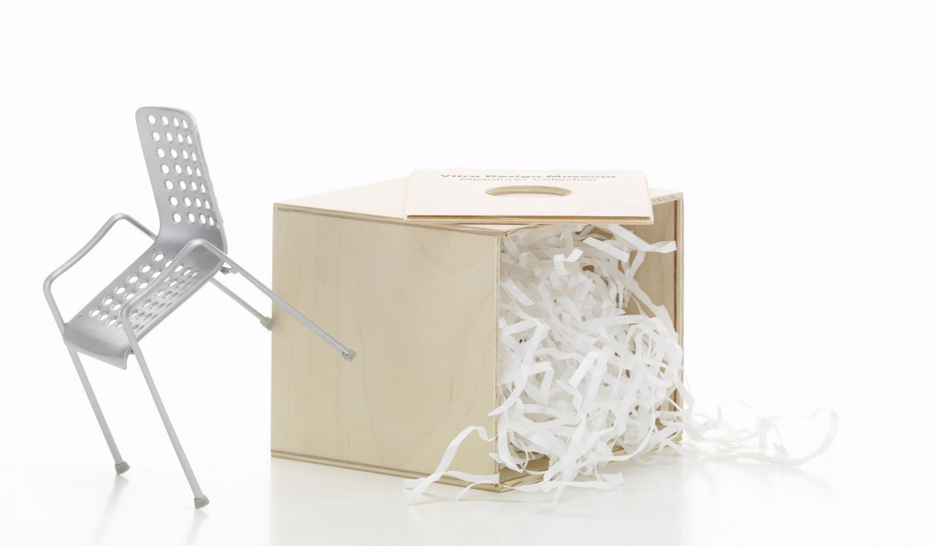 Landi Stuhl Miniatur von Vitra neben einer geöffneten Holzkiste mit Füllmaterial.