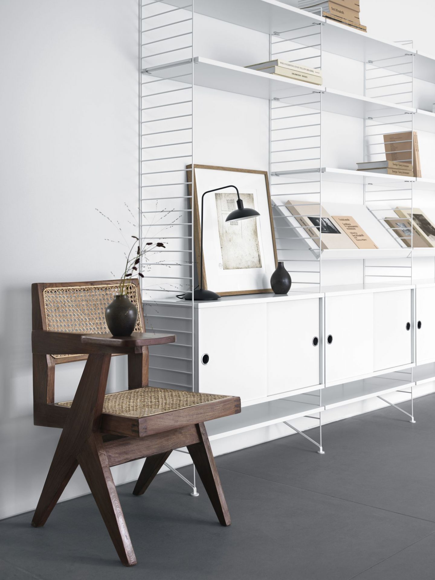 String Furniture Bodenleiter in Schwarz mit Regalsystem und Holzstuhl im Interieur.