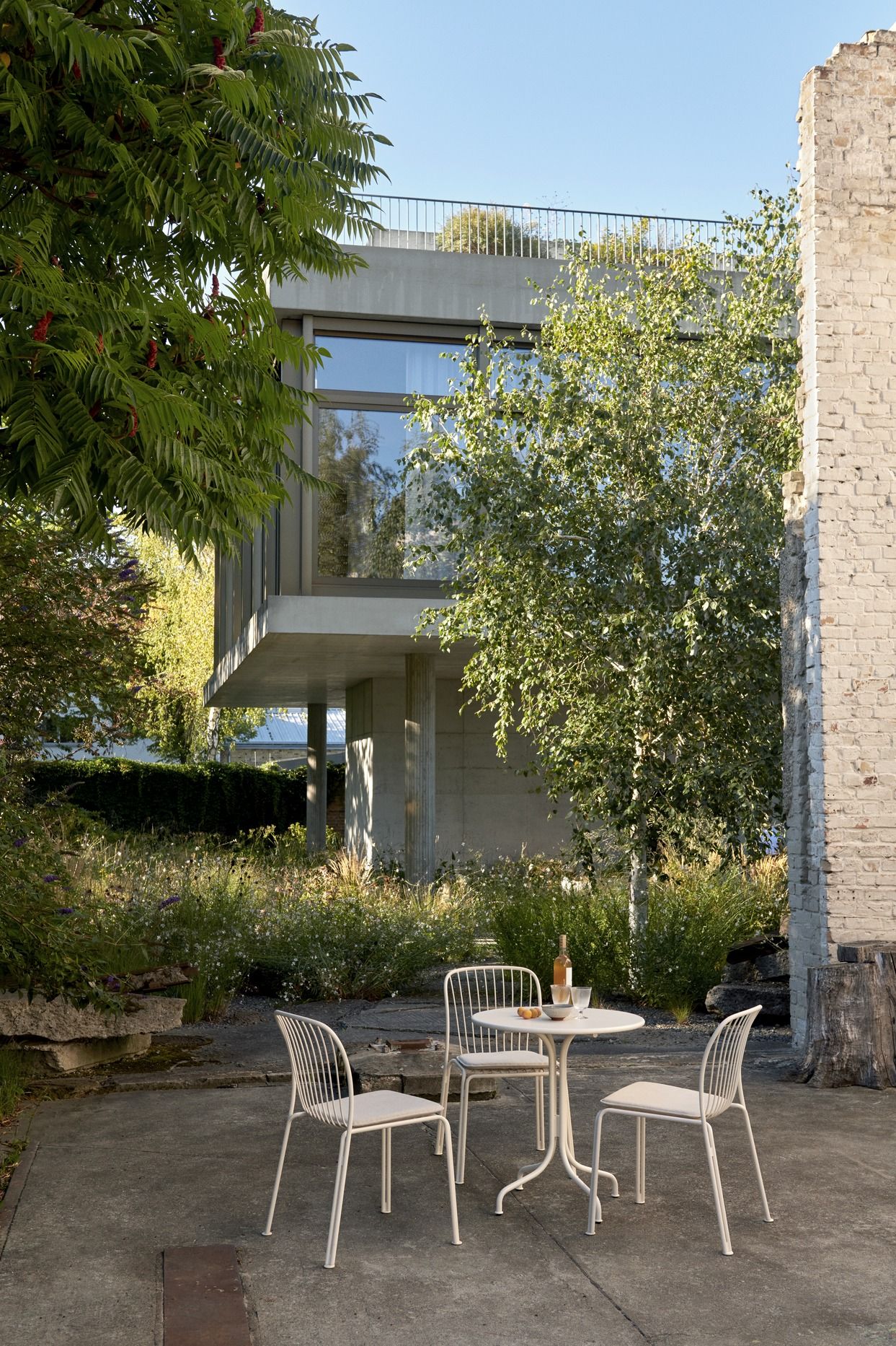 AndTradition Thorvald Gartentisch mit Stühlen im Außenbereich vor modernem Haus und Garten.