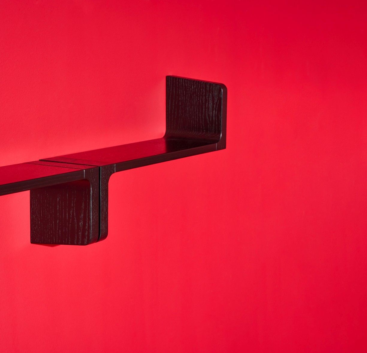 Schwarzes Ulna Wandregal von Schönbuch vor rotem Hintergrund, modernes Design Holzregal für Wohnzimmer.