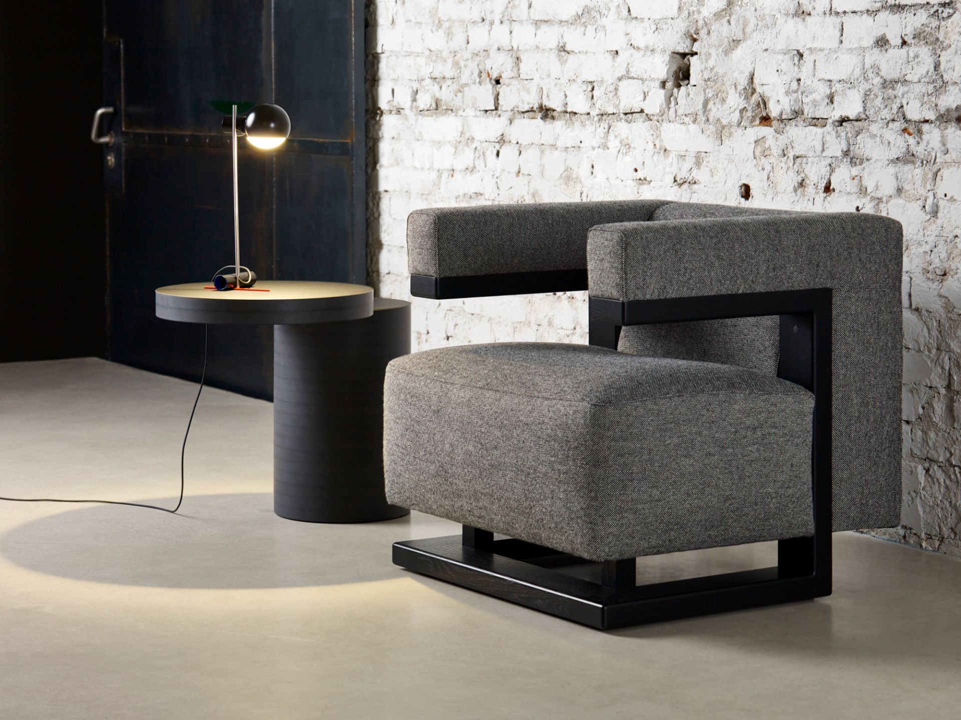 L25 Tischleuchte LED von Tecta, schwarz glänzend, auf einem runden Beistelltisch neben einem Sessel.