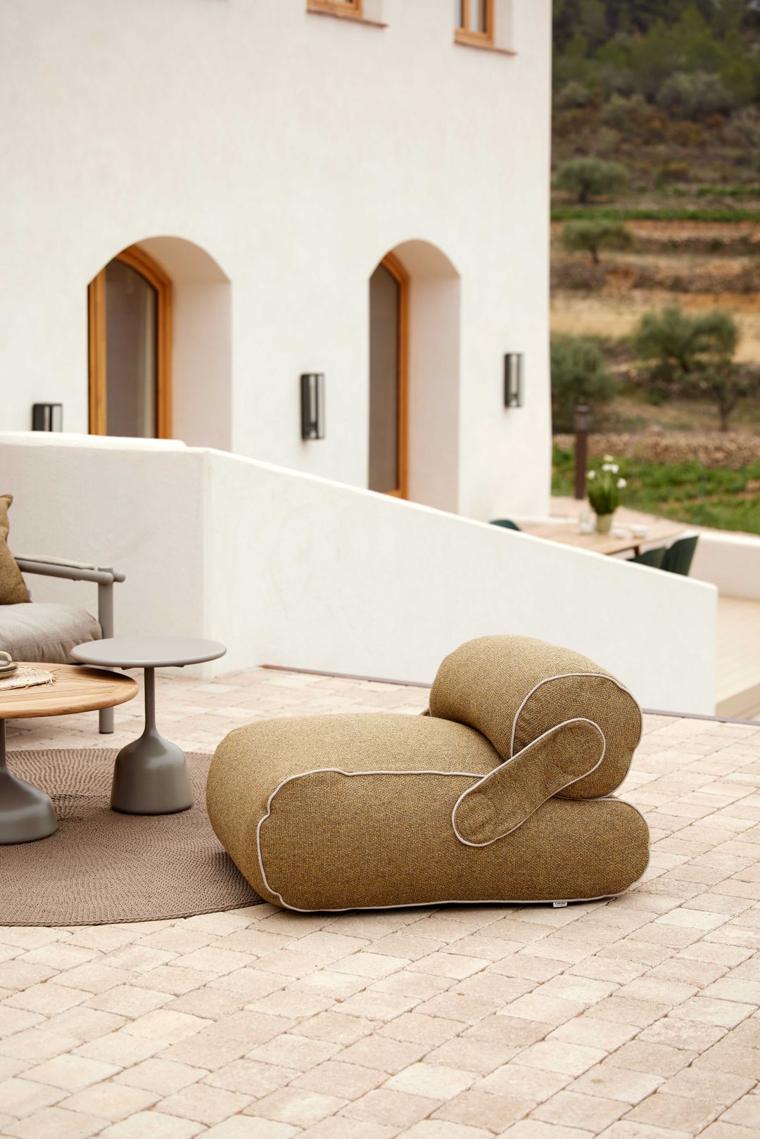 Nahaufnahme des Cane-Line Unite Outdoor Loungesessels in Beige mit weißen Akzenten auf einer Terrasse.