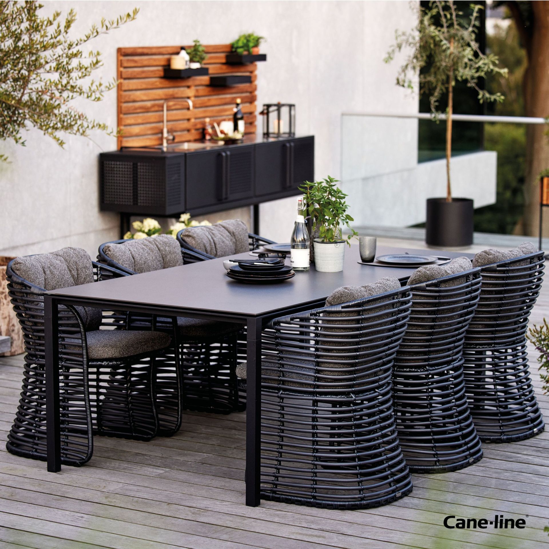 Cane-Line Basket Sessel Graphit mit grauen Kissen und Esstisch für den Garten.