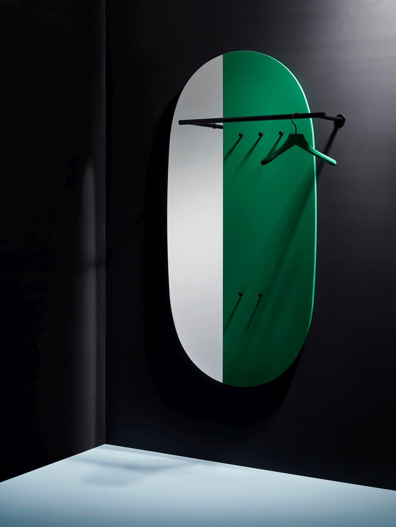 Grüne Schönbuch Mask Paneelgarderobe mit Kleiderbügel, Stange und Haken an dunkler Wand.