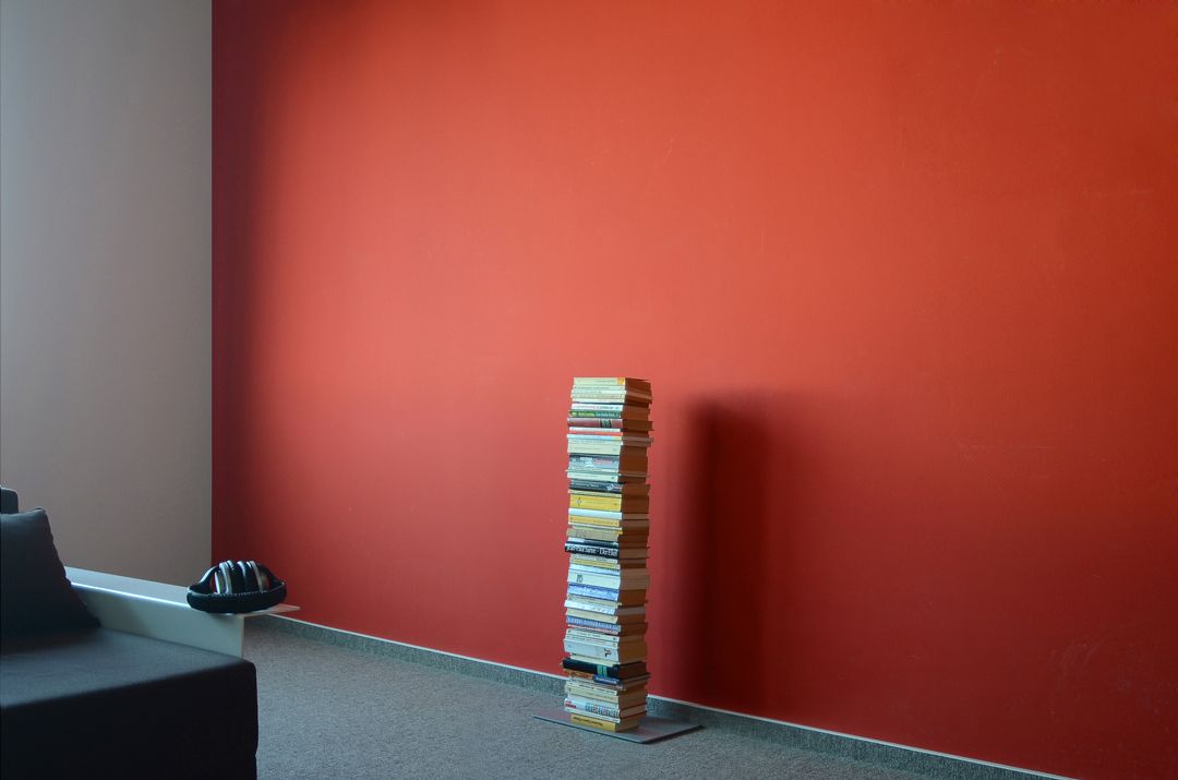 Booksbaum: Freistehendes Bücherregal mit gestapelten Büchern vor roter Wand. Einzel Standregal.
