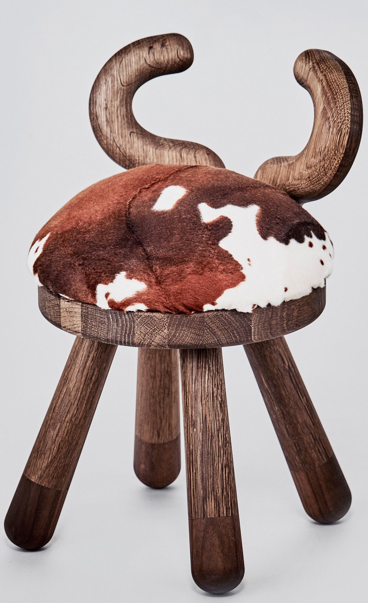 Dreibeiniger Kinderstuhl "Cow Chair" mit Kuhfell-Sitzfläche und hölzerner Rückenlehne in Form von Hörnern.