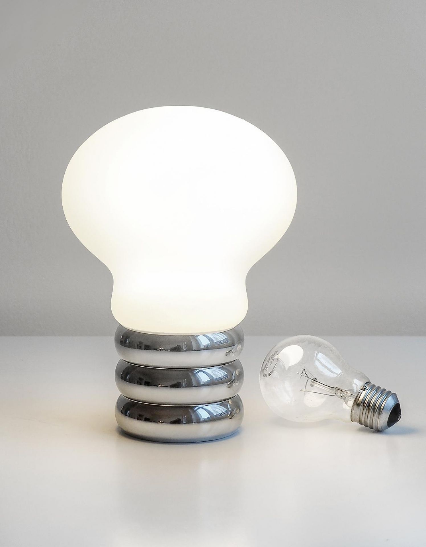 b.bulb Akkuleuchte von Ingo Maurer: Tischleuchte mit USB-Anschluss, glänzendem Chromfuß und leuchtendem Glühbirnen-Design.