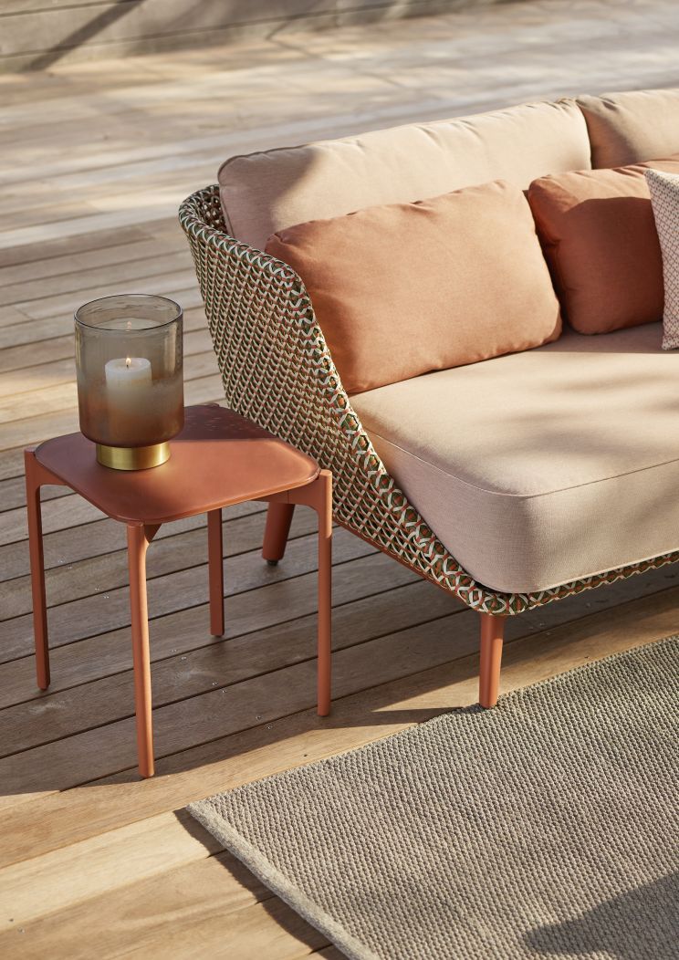 Rechteckiger Izon Beistelltisch von Dedon in Terrakotta neben einem Outdoor-Sofa mit Kissen und Kerze.