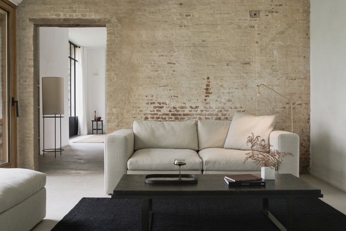 Helles Ethnicraft Sofa "Mellow" als 2,5-Sitzer im Wohnzimmer mit Ziegelwand und dunklem Teppich.