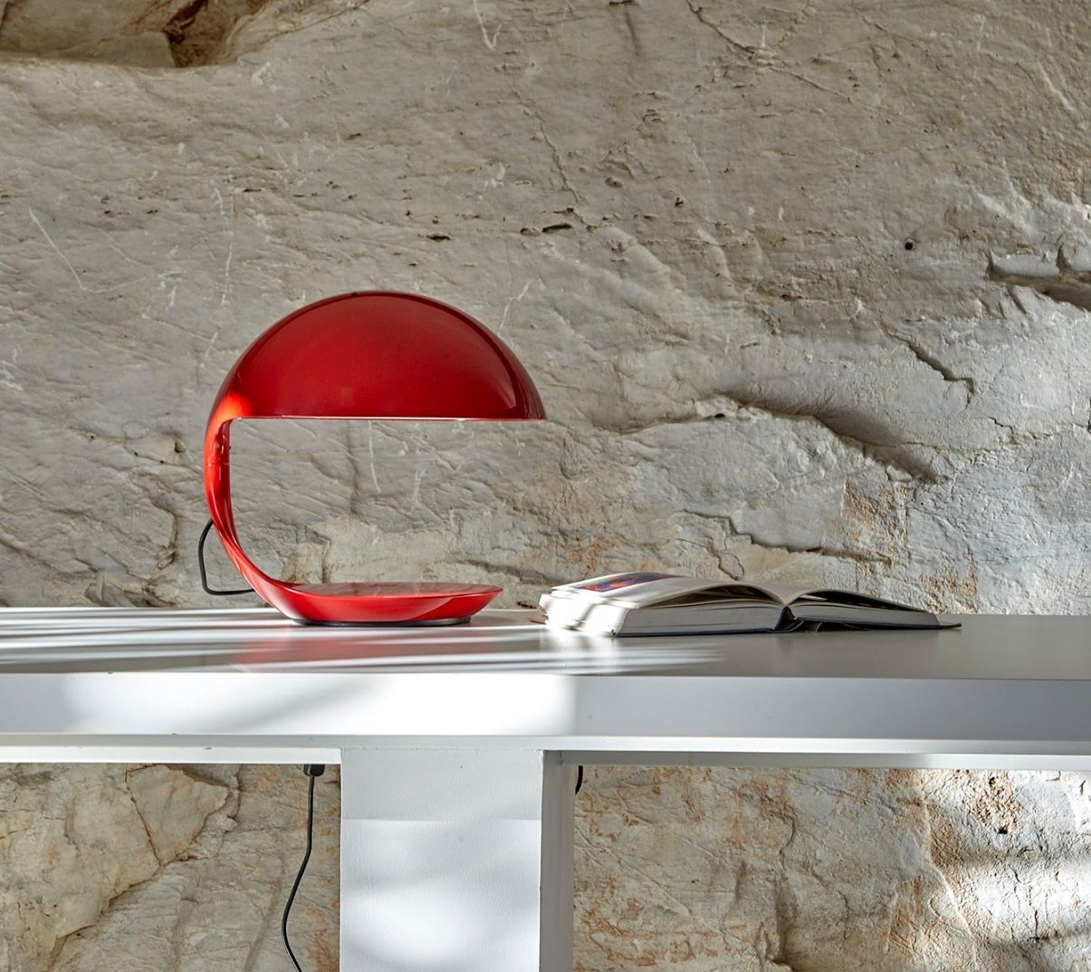 Rote Cobra Tischleuchte von Martinelli Luce neben einem offenen Buch auf einem weißen Tisch.