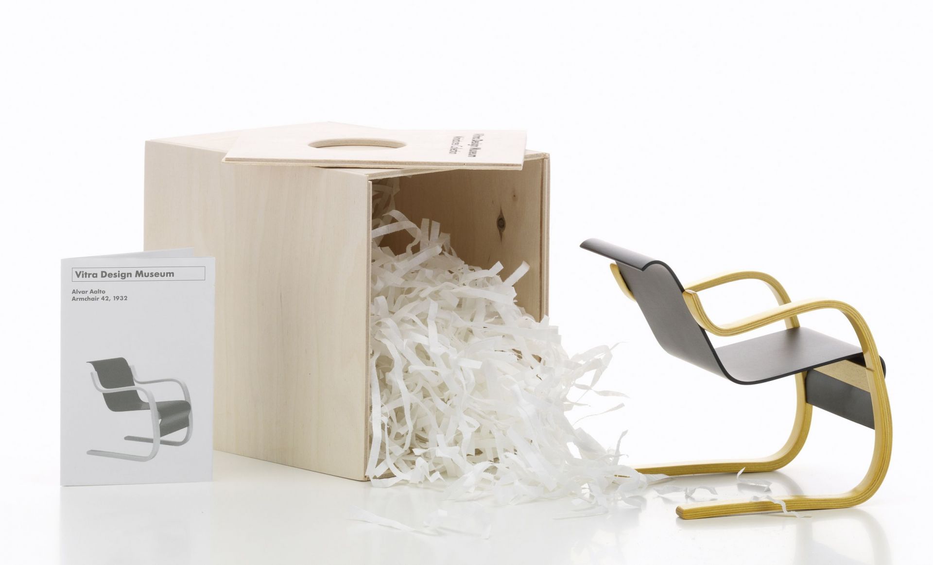Miniatur Vitra Armchair Nr. 42 Sessel aus Holz, neben einer Holzkiste mit Füllmaterial.