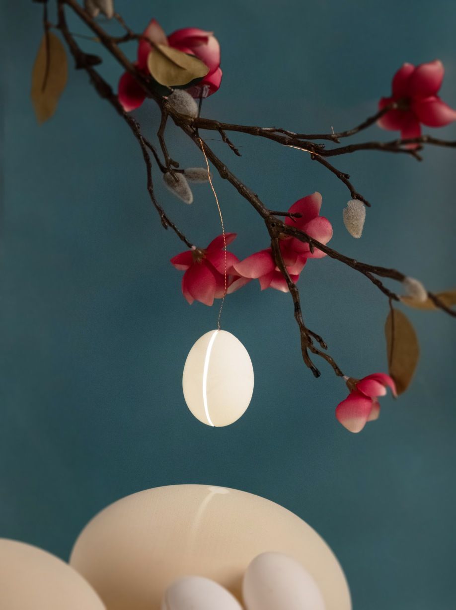 Reality Pendelleuchte: Ei-förmige Hängelampe von Ingo Maurer, dekoriert mit blühenden Zweigen, modernes Design.