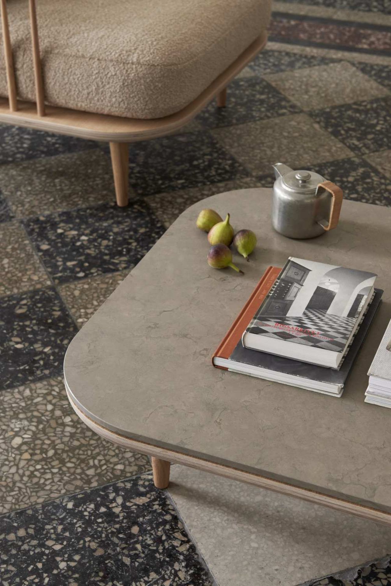 AndTradition Fly Table Couchtisch mit Büchern, Feigen und Teekanne auf gemustertem Boden.
