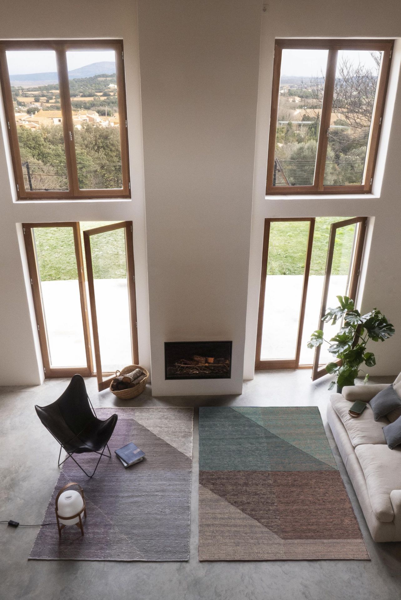 Zwei Nanimarquina Capas Teppiche 170x240 cm im modernen Wohnzimmer mit Sessel und Kamin. Designteppiche für stilvolles Wohnen.