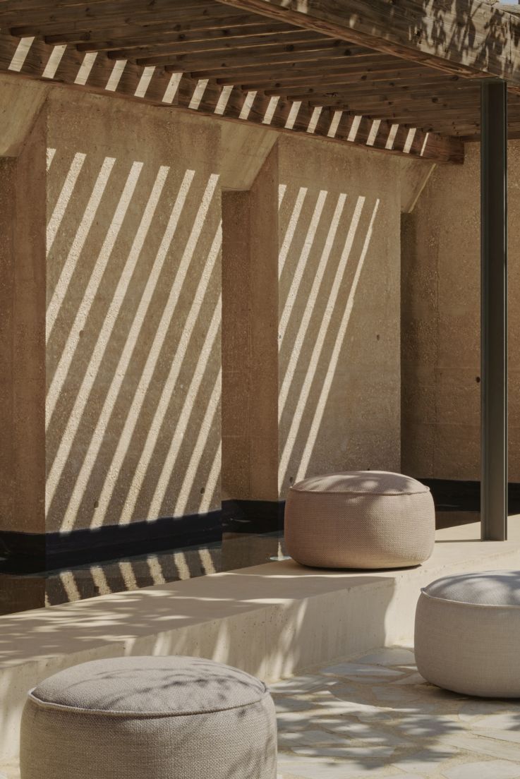 Drei graue Outdoor Sitzhocker im Donut-Design von Ethnicraft vor einer Wand mit Schattenmuster.