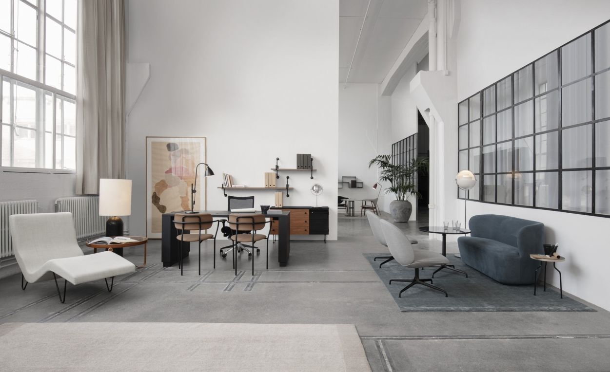 Heller Raum mit Gubi Stehleuchte, Schreibtisch, Stühlen und Sofa. Designermöbel für Büro und Wohnen.