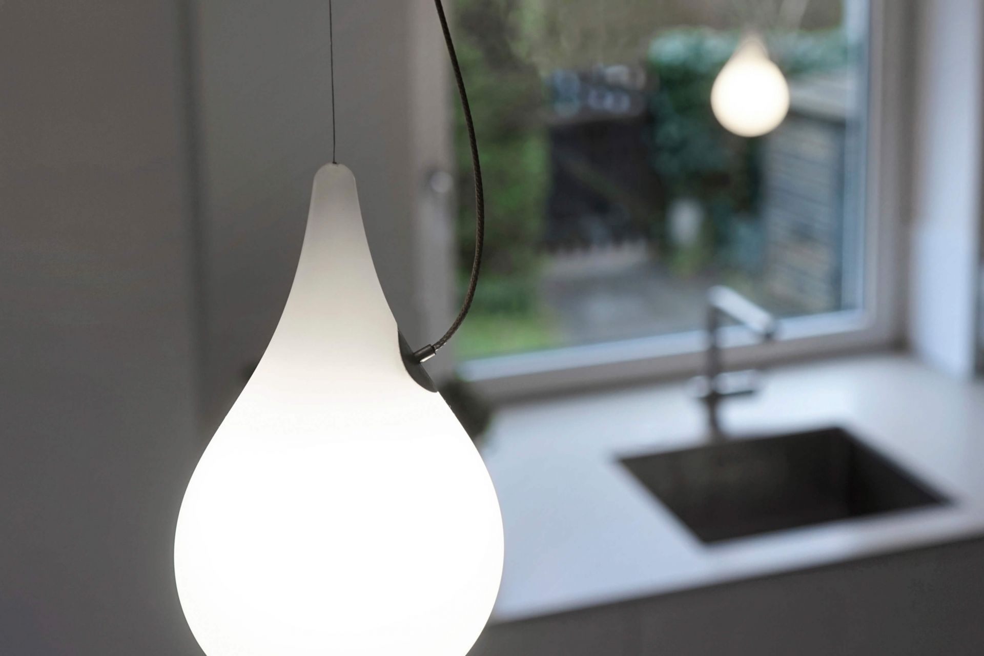 Nahaufnahme der Liquid Light Pendelleuchte von Next, Tropfenform, modernes Design, warmes Licht.