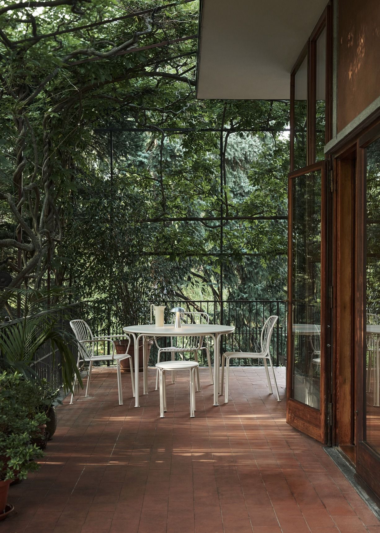 AndTradition Thorvald Stuhl SC94 für den Außenbereich auf einer Terrasse mit Tisch und Pflanzen.