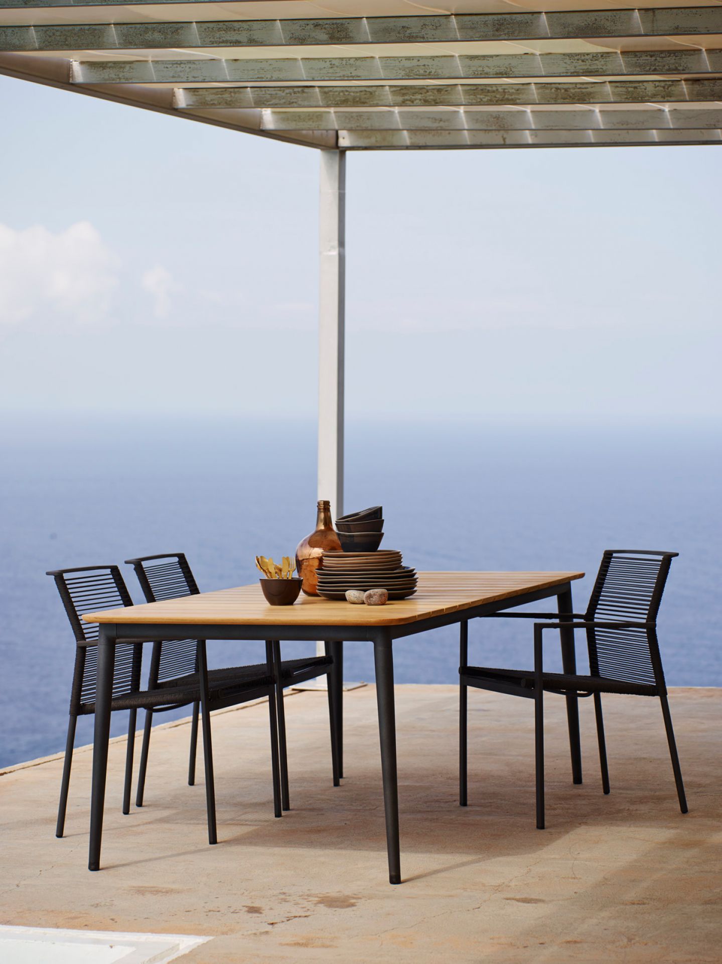 Edge Outdoor Sessel von Cane-Line, stapelbar, mit Tisch und Geschirr auf einer Terrasse.