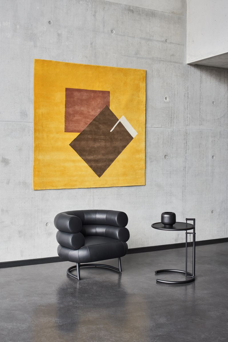 Gelber Castellar Teppich von ClassiCon (300x250cm) mit braunen geometrischen Formen an einer Betonwand.