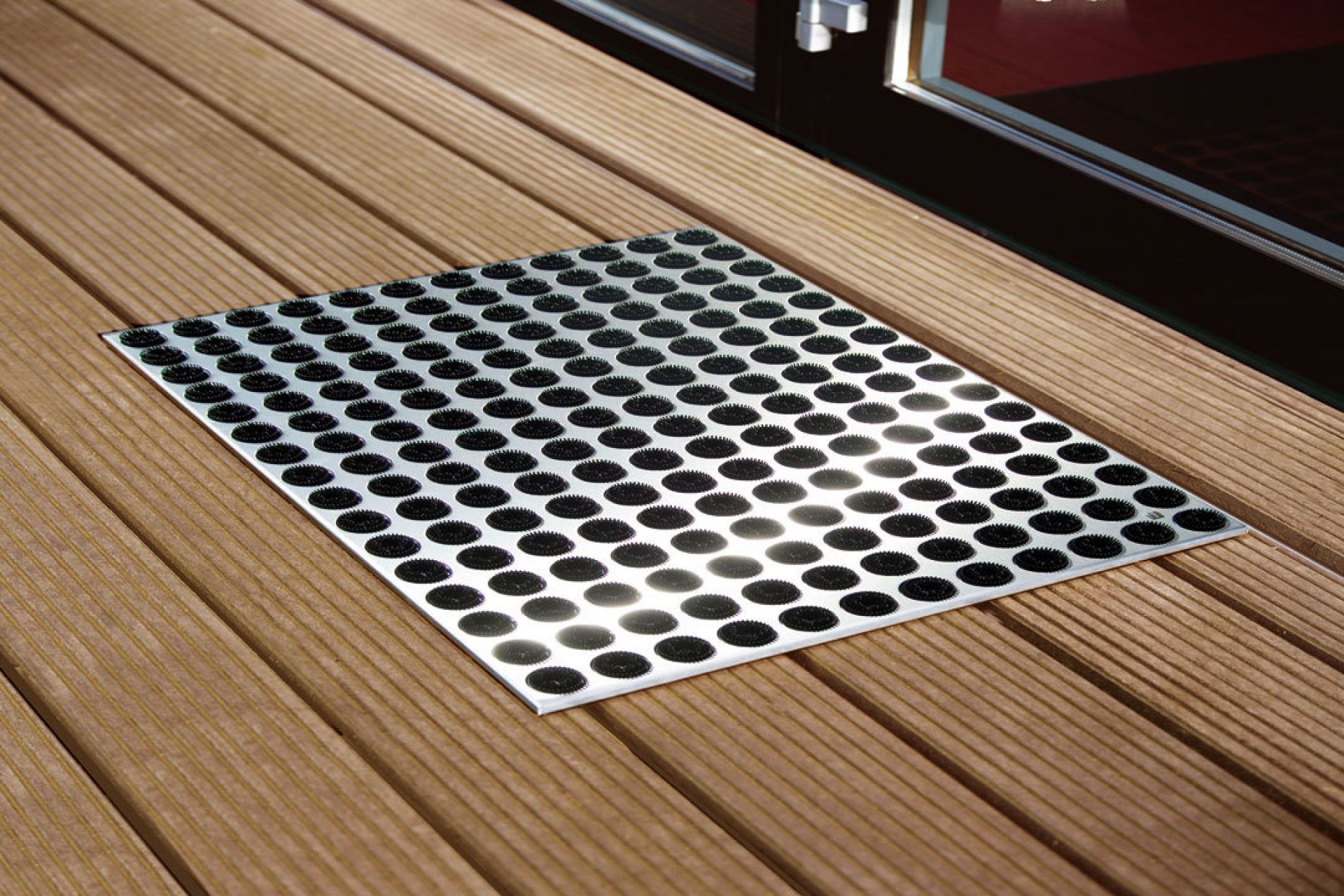 Feet-Back Fußmatte auf Holzterrasse, silberne Oberfläche mit schwarzen Noppen, Schmutzfangmatte für den Außenbereich.