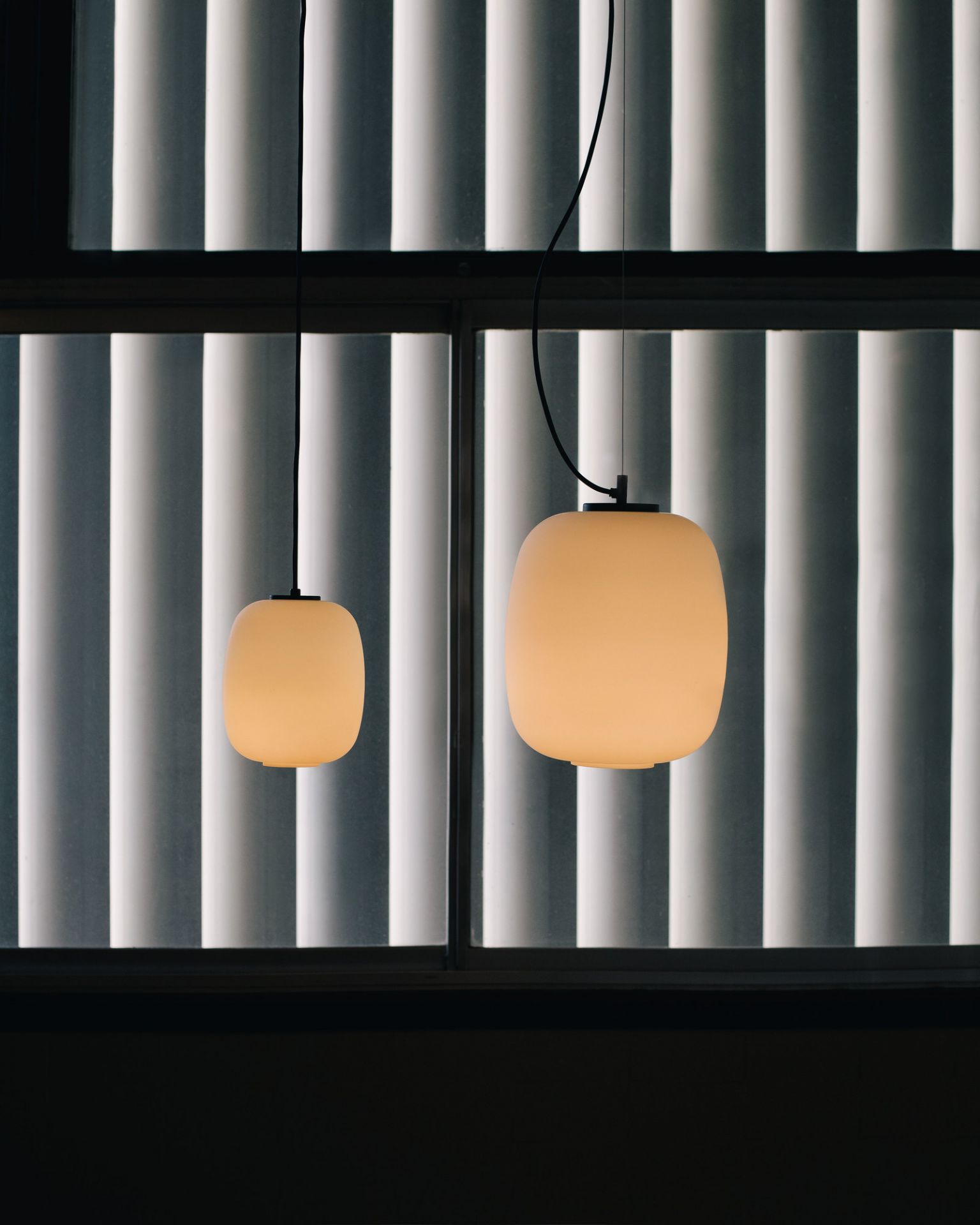 Zwei Globo Cesta Pendelleuchten von Santa & Cole vor einem Fenster mit Jalousien.