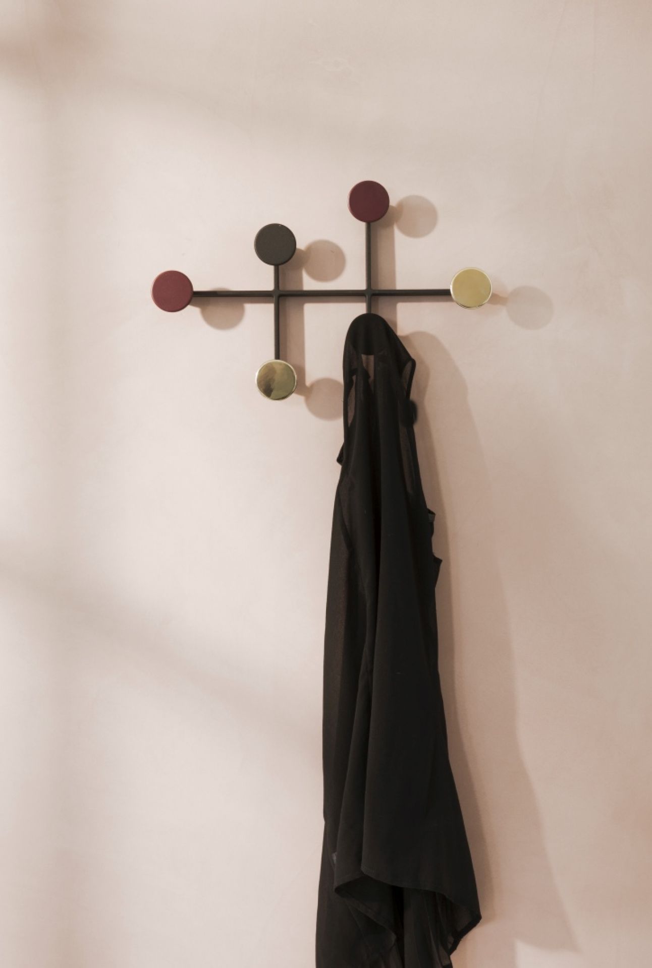 Schwarzer Afteroom Coat Hanger Garderobenhaken mit farbigen Knöpfen und hängender Kleidung vor rosa Wand.