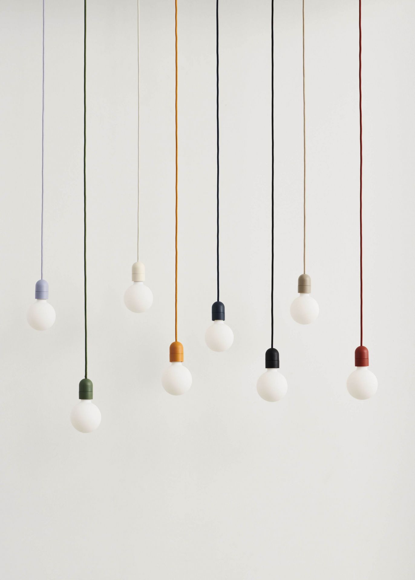 Mehrere Hay Pendelleuchten mit farbigen Textilkabeln und Fassungen, darunter rostrot, für moderne Innenbeleuchtung.