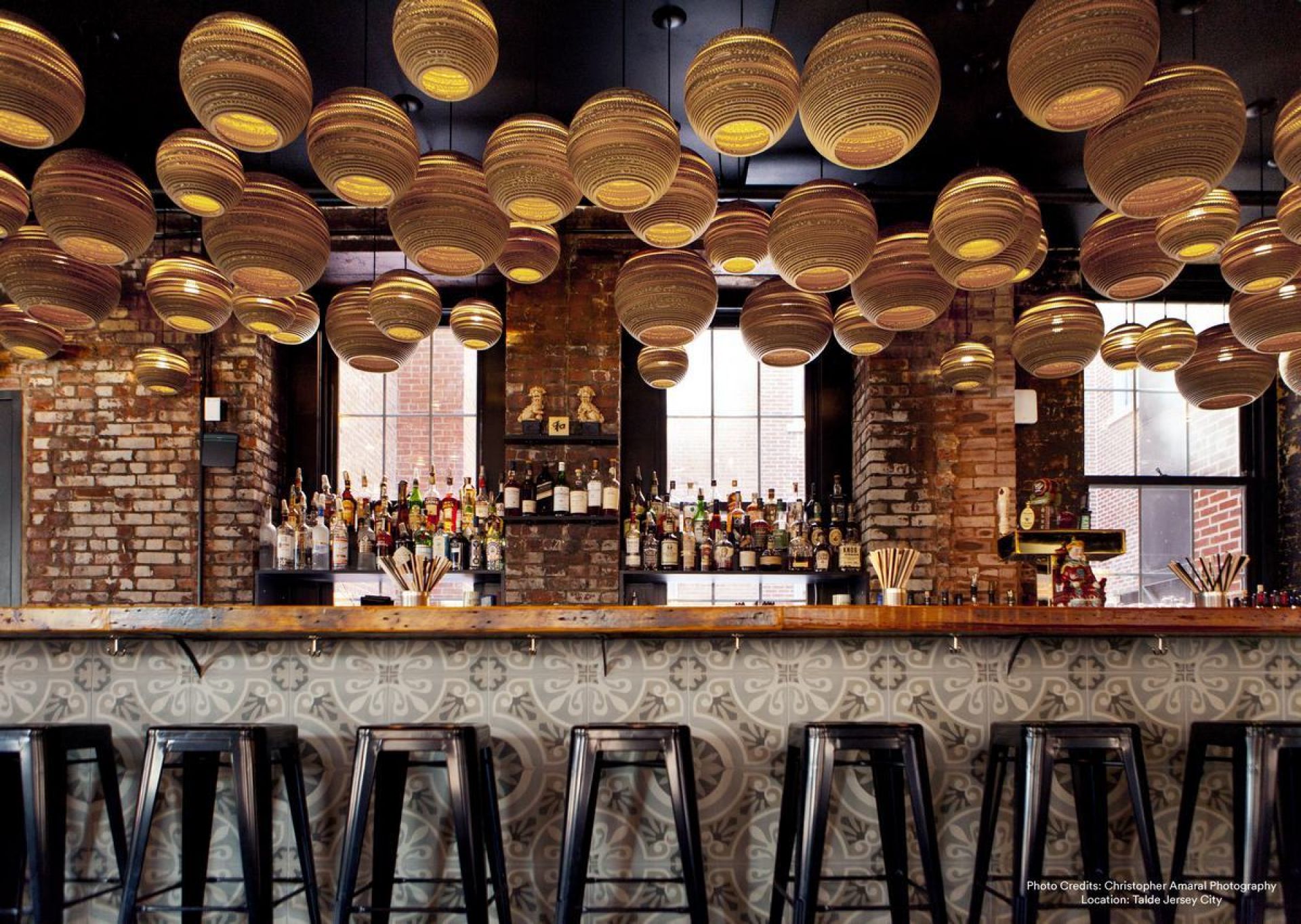 Viele Moon10 Scraplights Hängeleuchten von Graypants in einem Raum mit Bar und Backsteinwänden.