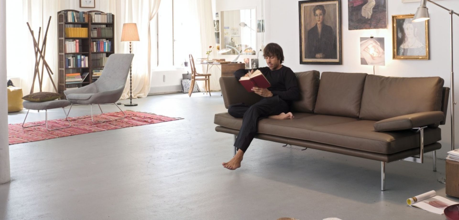 Mann liest auf braunem Ledersofa von Walter Knoll mit verstellbaren Armlehnen. Wohnzimmer-Szene.