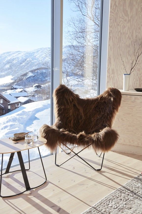 Iceland Mariposa Butterfly Chair Sessel mit braunem Schaffellbezug vor verschneiter Landschaft. Gemütlicher Ledersessel.