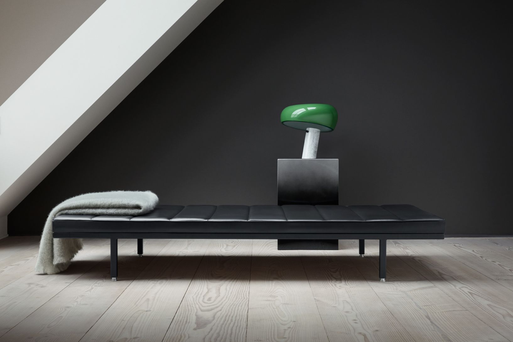Schwarzes Vipp Daybed mit gesteppter Lederauflage, Wolldecke und grüner Lampe auf einem Holzboden.