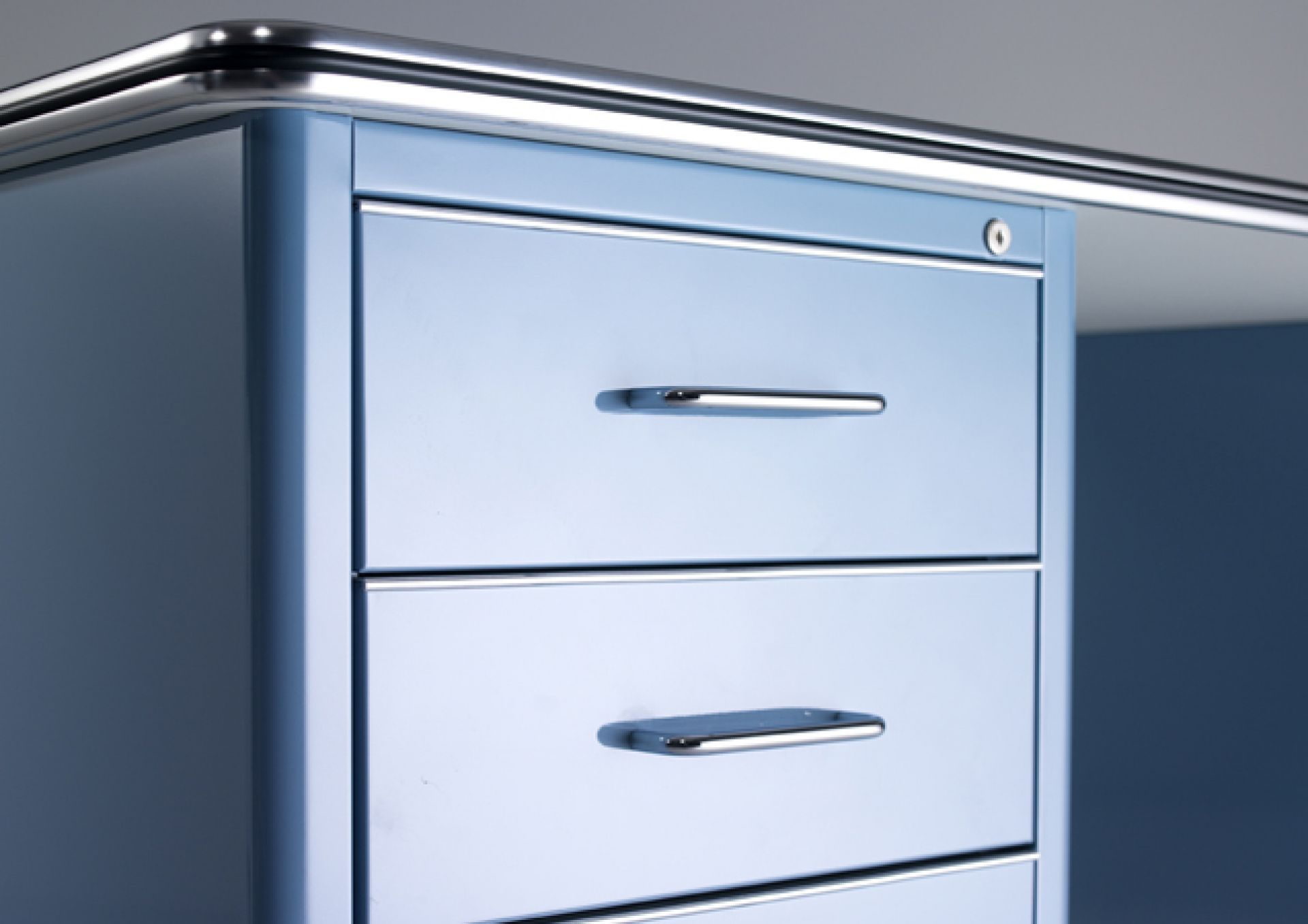 Detailaufnahme des blauen TB 228 Classic Line Schreibtischs von Müller Möbelfabrikation mit drei Schubladen und Chromgriffen.