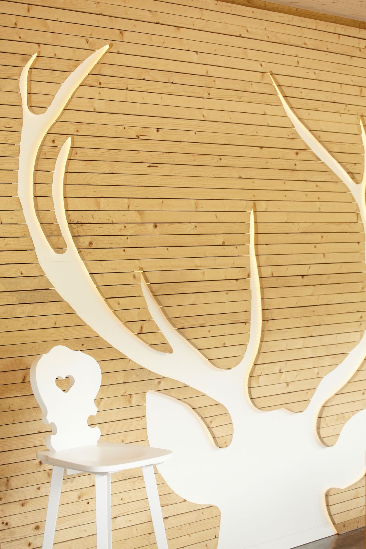 Weißer Jan Kurtz Vienna Stuhl vor Holzwand mit Hirschgeweih-Dekoration, skandinavisches Design.