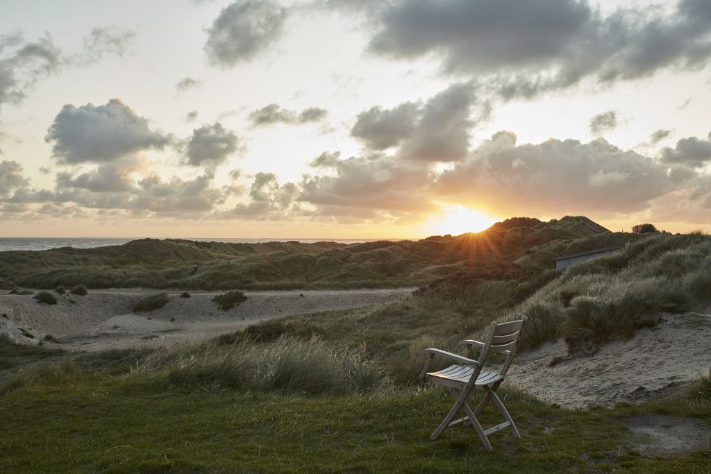 Selandia Armchair Outdoor Sessel vor Dünenlandschaft bei Sonnenuntergang. Skagerak Gartenmöbel für entspannte Stunden.