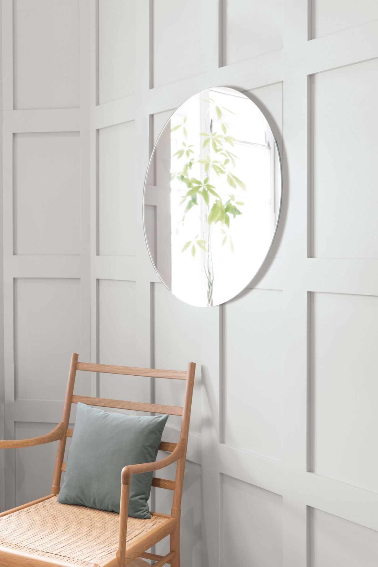Runder Schönbuch Spiegel, Durchmesser 75 cm, an weißer Wand über einem Holzstuhl.