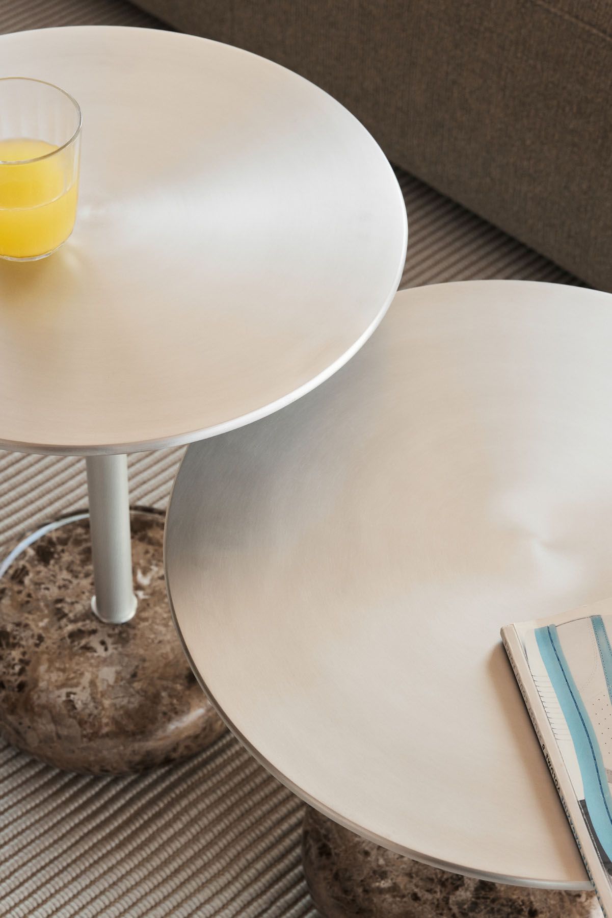 Nahaufnahme von zwei runden Northern Ton Beistelltischen H50cm mit Marmorfuß, einer mit Orangensaft.