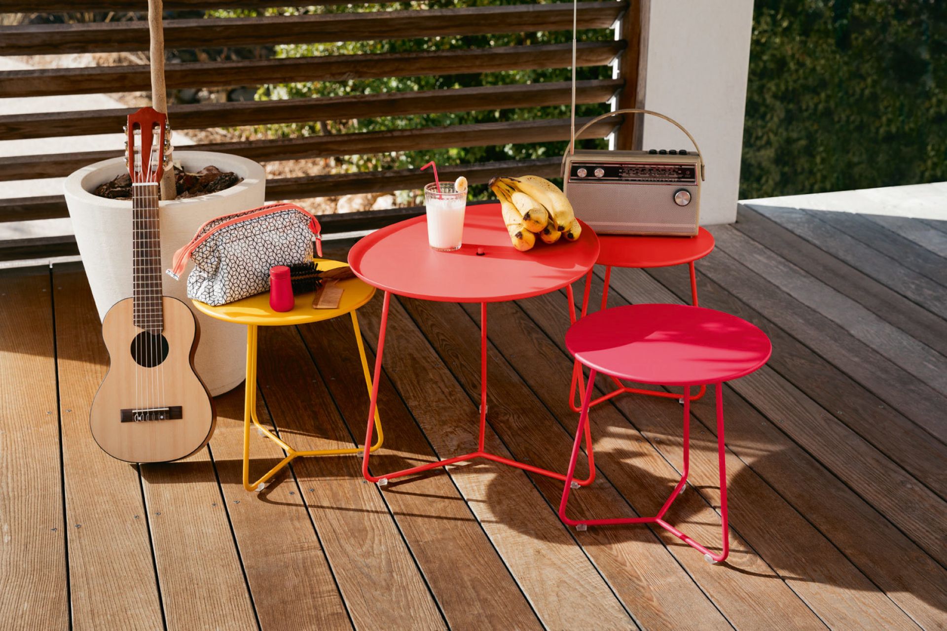 Kleiner, runder Outdoor Tisch von Fermob in verschiedenen Farben auf einer Holzterrasse.