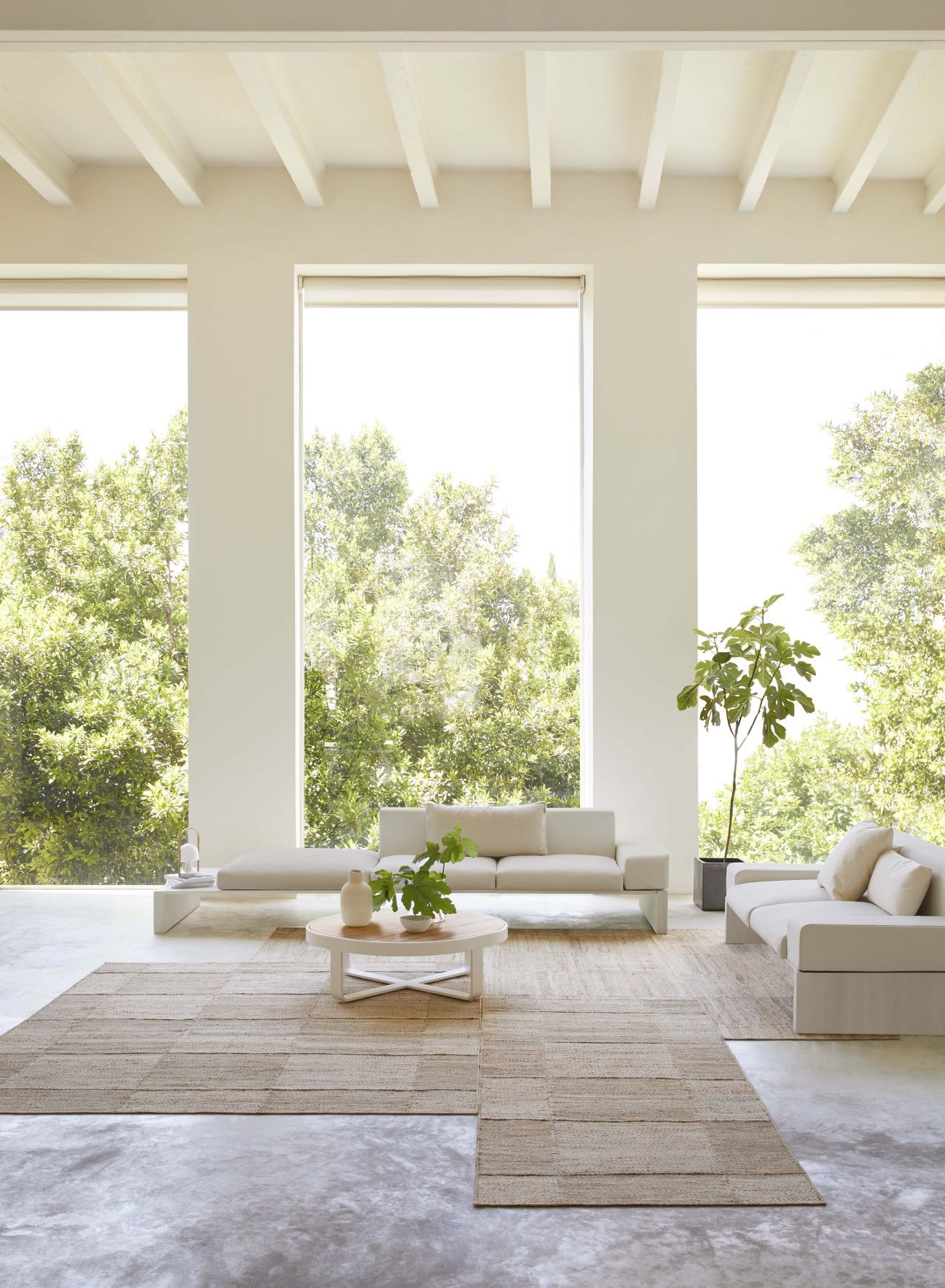 Wohnzimmer mit hellem Roots Teppich von Gan, Sofa und großem Fenster für natürliches Licht.