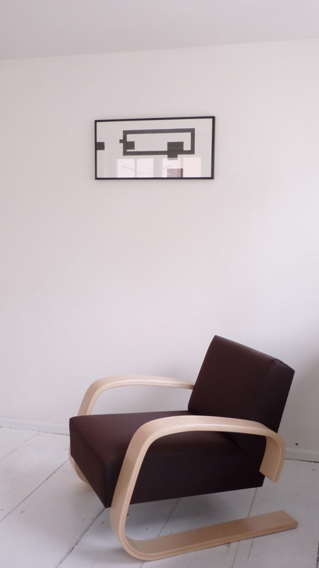 Brauner Artek Sessel mit gebogenen Holzrahmen vor weißer Wand und abstraktem Bild.