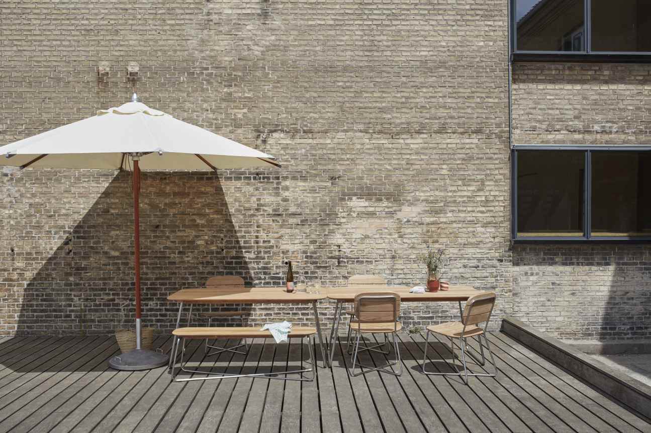 Atlantis Sonnenschirm von Skagerak: Eleganter, goldgelber Gartenschirm spendet Schatten über einer modernen Sitzgruppe im Freien.