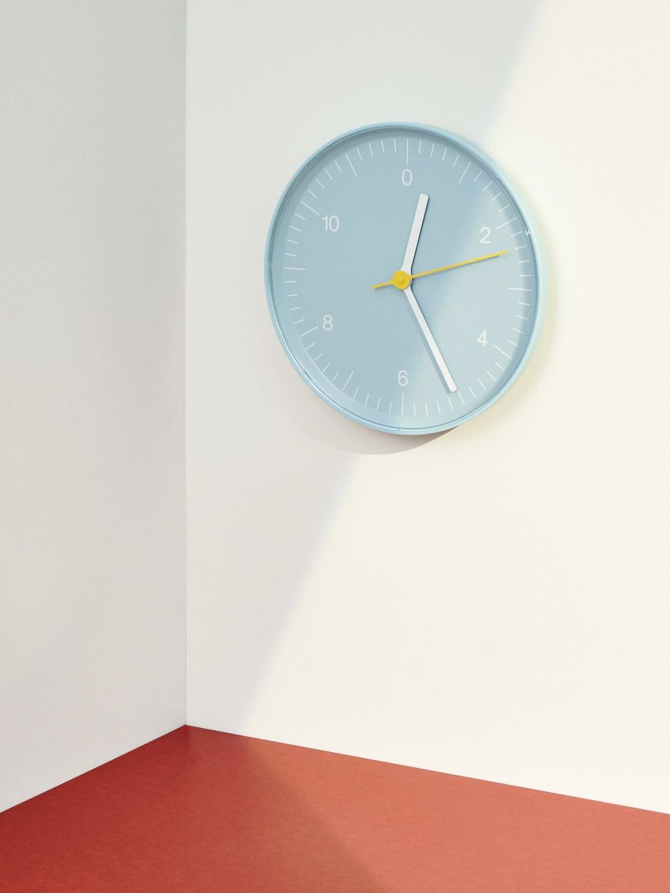 Helle Hay Wanduhr in Pastellblau mit gelben Akzenten an einer weißen Wand.