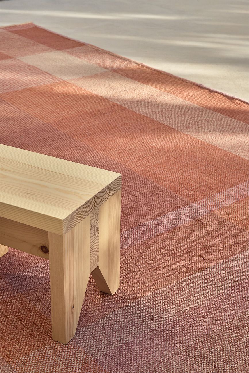 Nahaufnahme des Nanimarquina Teppichs Nuance in Lime mit geometrischem Muster und Holzbank.