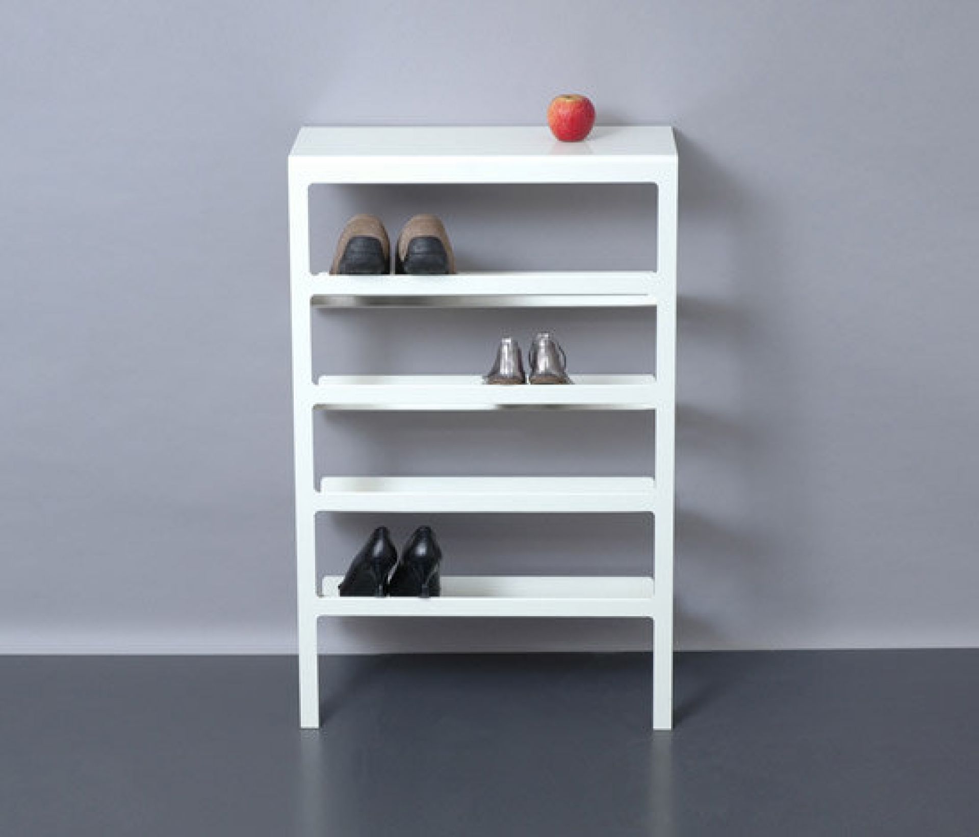 Weißes Mila Schuhregal Mox mit vier Ablagen, darauf Schuhe und ein Apfel.