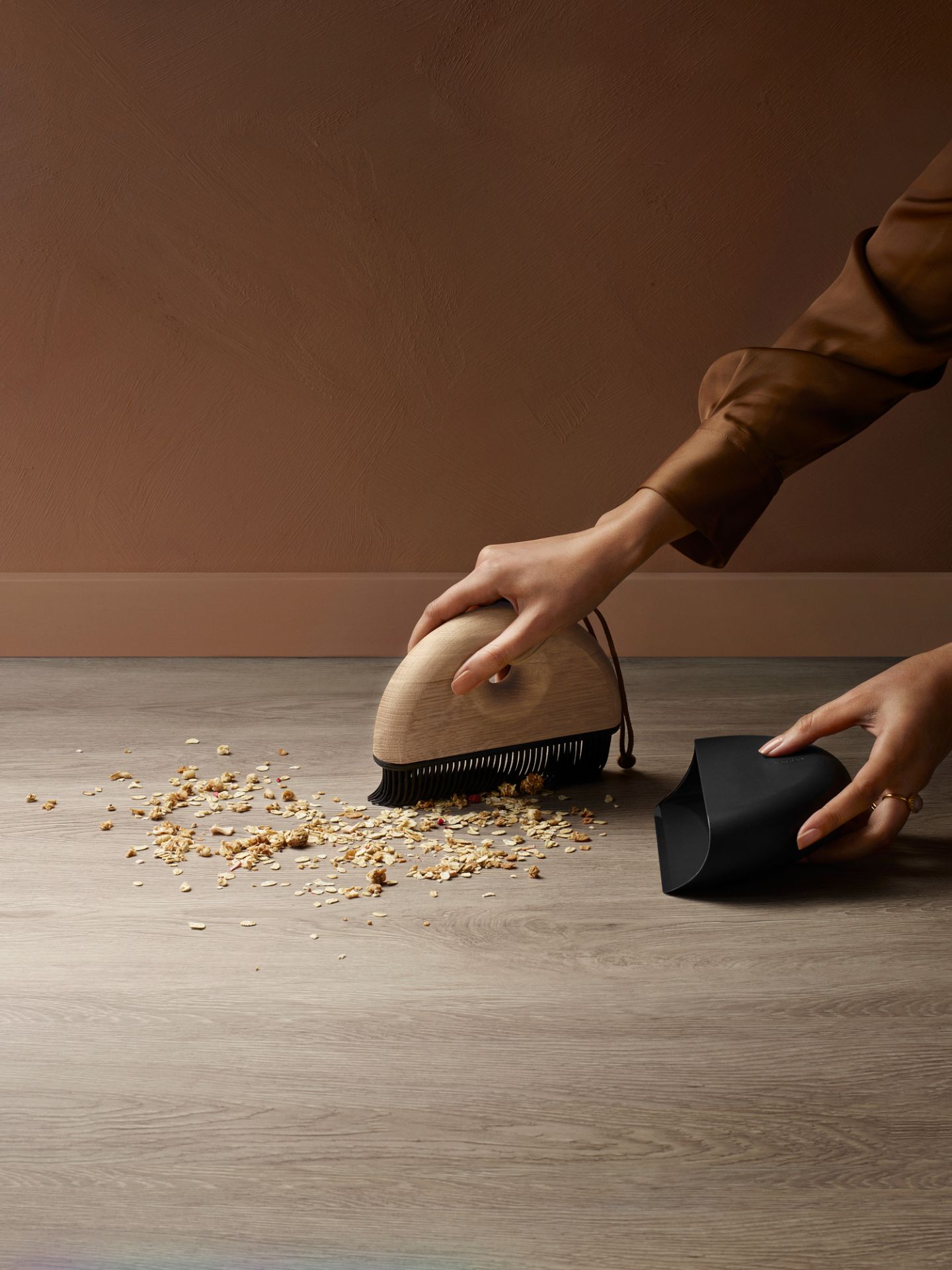Frau kehrt Krümel mit Eva Solo Handfeger und Kehrblech Set vom Holzboden auf.