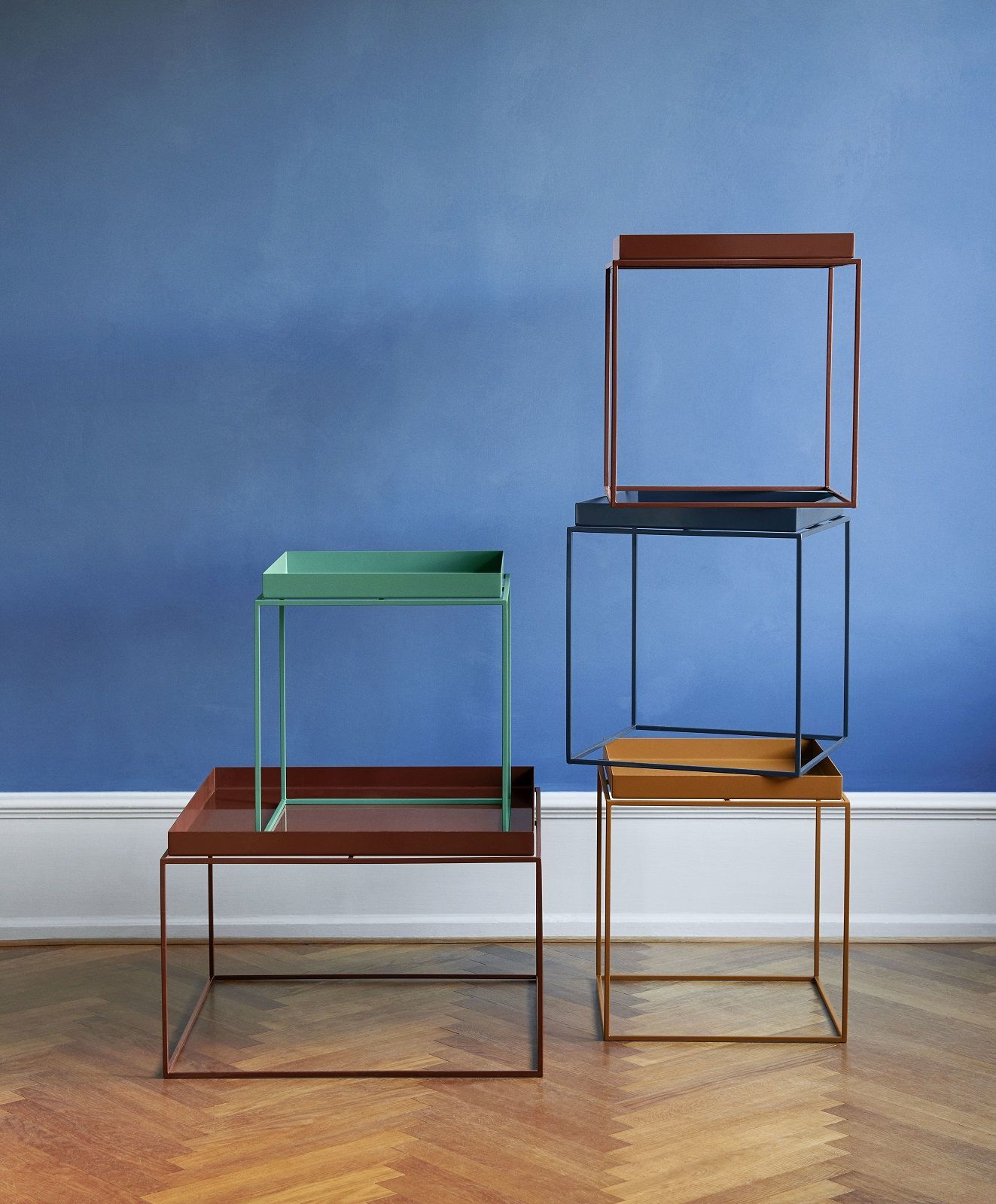 Hay Tray Table Couchtische in verschiedenen Farben gestapelt vor blauem Hintergrund, modernes Wohnzimmer-Design.
