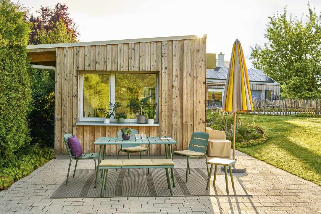 Weishäupl Gartenmöbel-Set auf Terrasse mit Vapio Stool Hocker, Tisch, Bank und Stühlen in grüner Farbe.